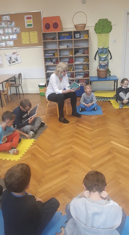 Zdjęcie przedstawia nauczycielkę czytającą książkę dzieciom.