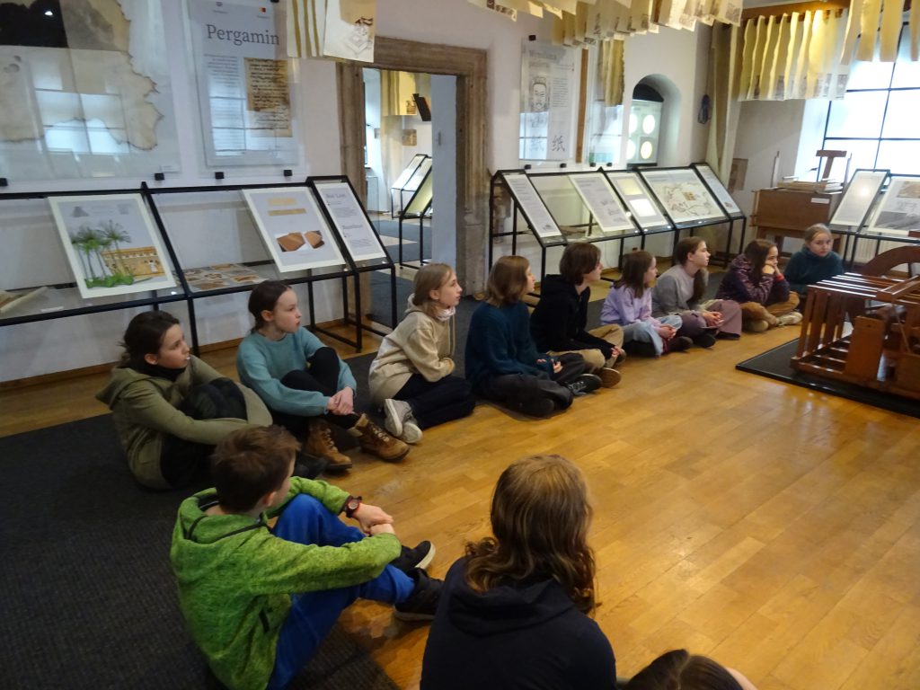 Zwiedzanie Muzeum Papiernictwa. Uczniowie siedzą i słuchają przewodnika.